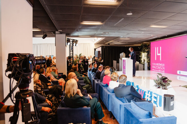 Wojewoda Mazowiecki przemawia ze sceny podczas 14. Forum Rozwoju Mazowsza. Na widowni licznie zgromadzeni uczestnicy wydarzenia, a w tle widoczna oprawa multimedialna z logo Forum i motywem „Mazowsze 20 lat w UE”.