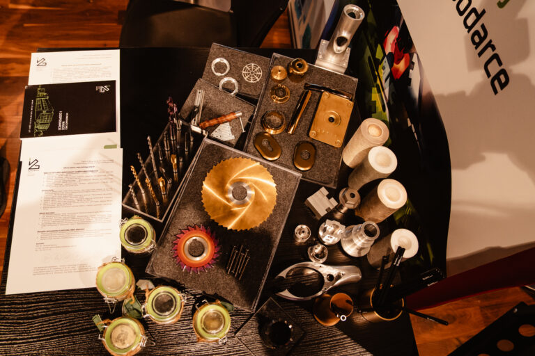 Stoisko Sieci Badawczej Łukasiewicz podczas 14. Forum Rozwoju Mazowsza. Na stole zaprezentowano elementy metalowe, narzędzia i próbki technologiczne wykorzystywane w badaniach przemysłowych i innowacjach inżynieryjnych.