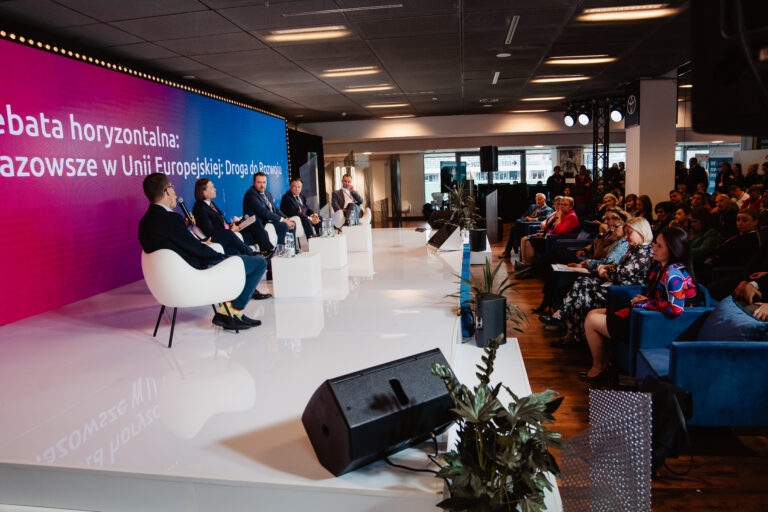 Debata horyzontalna „Mazowsze w Unii Europejskiej: Droga do rozwoju” podczas 14. Forum Rozwoju Mazowsza. Na scenie kilku prelegentów siedzących w białych fotelach, omawia kierunki rozwoju regionu. W tle duży ekran z nazwą panelu, a na widowni uczestnicy wydarzenia uważnie słuchają dyskusji.