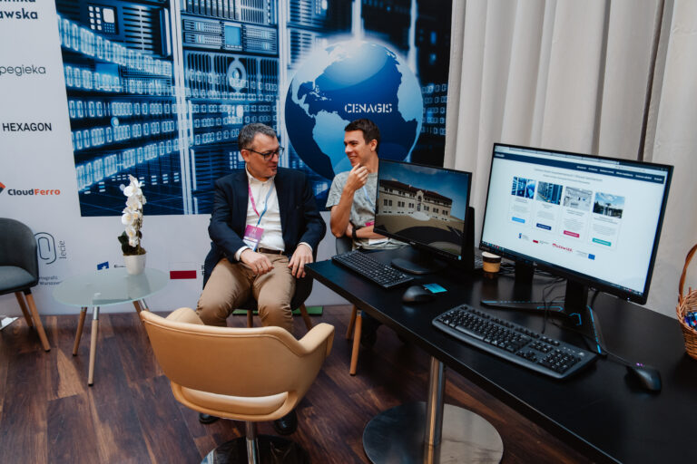 Stoisko CENAGIS podczas Forum Rozwoju Mazowsza, dwie osoby rozmawiają przy komputerach z wizualizacjami projektów.