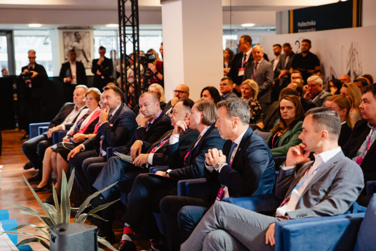 Uczestnicy 14. Forum Rozwoju Mazowsza siedzący w pierwszych rzędach podczas sesji plenarnej. Słuchają wystąpienia na głównej scenie, w tle widoczni pozostali goście wydarzenia oraz obsługa medialna.