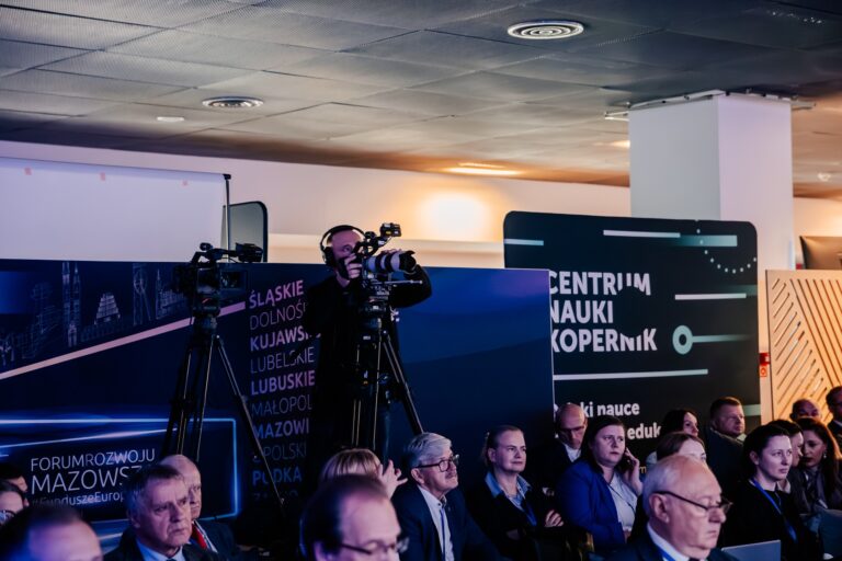 Operator kamery transmituje wydarzenie „Forum Rozwoju Mazowsza” w sali z tablicą „Centrum Nauki Kopernik”