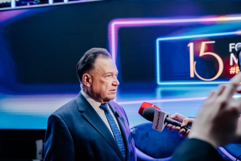 marszałek Adam Struzik udziela wywiadu przed mikrofonami, w tle podświetlona ścianka z napisem „15 Forum Rozwoju Mazowsza”