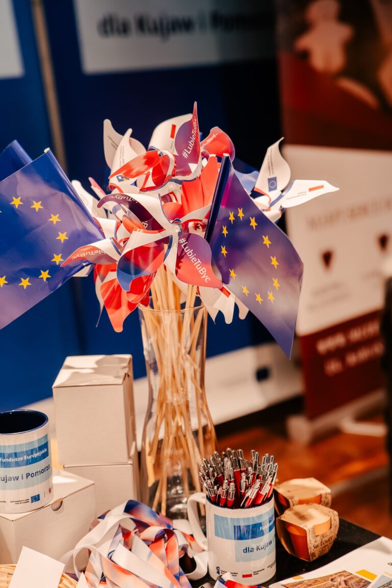 Stoisko Województwa Kujawsko-Pomorskiego podczas 15. Forum Rozwoju Mazowsza – gadżety promocyjne z logo programu „dla Kujaw i Pomorza” oraz Unii Europejskiej, symbolizujące wsparcie regionu z funduszy europejskich.