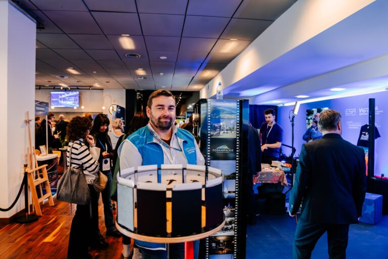 Stoisko Województwa Podkarpackiego podczas 15. Forum Rozwoju Mazowsza. W centrum zdjęcia znajduje się przedstawiciel ekspozycji, a wokół uczestnicy wydarzenia oglądają prezentacje i instalacje multimedialne.