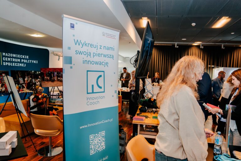Uczestnicy 15. Forum Rozwoju Mazowsza przy stoisku programu Innovation Coach prowadzonego przez Instytut Podstawowych Problemów Techniki PAN. Na banerze widnieje hasło „Wykreuj z nami swoją pierwszą innowację