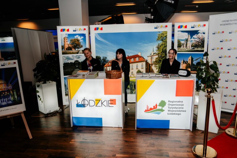 Stoisko województwa łódzkiego podczas 15. Forum Rozwoju Mazowsza. Przedstawiciele Regionalnej Organizacji Turystycznej prezentują ofertę regionu na tle zdjęć zabytków i krajobrazów Łódzkiego.