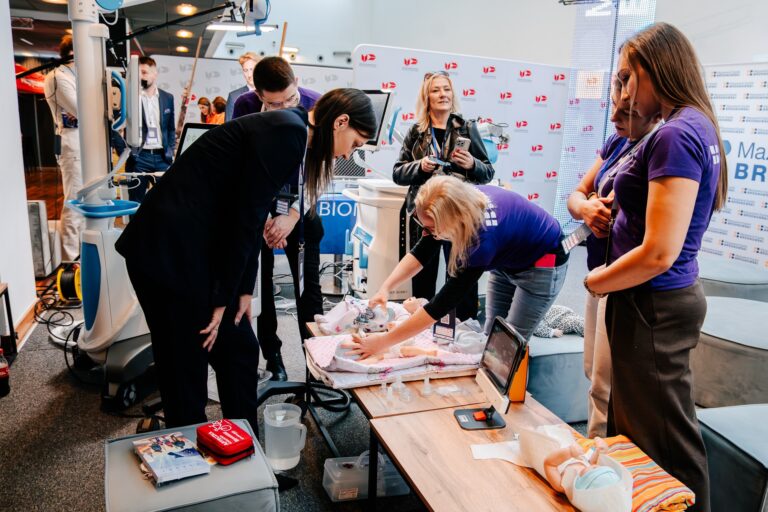 Pokaz udzielania pierwszej pomocy niemowlęciu podczas 15. Forum Rozwoju Mazowsza. Instruktor używa fantomu i sprzętu medycznego do demonstracji resuscytacji