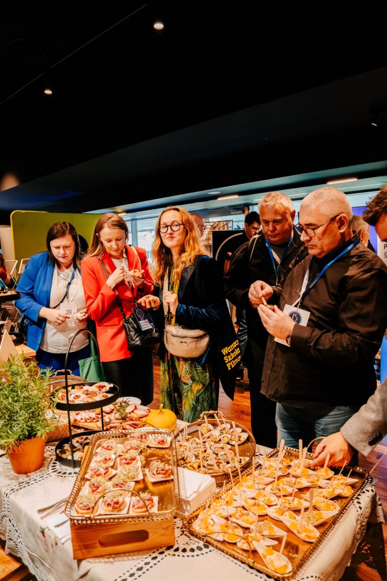Uczestnicy 15. Forum Rozwoju Mazowsza degustują regionalne potrawy przy stoisku z lokalnymi przysmakami – rozmowy i wymiana wrażeń odbywają się w swobodnej, przyjaznej atmosferze.
