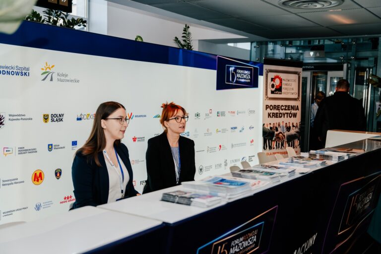 Główny Punkt Informacyjny Funduszy Europejskich podczas 15. Forum Rozwoju Mazowsza – dwie kobiety obsługujące stanowisko informacyjne, przy którym dostępne są materiały o możliwościach wsparcia z funduszy unijnych.
