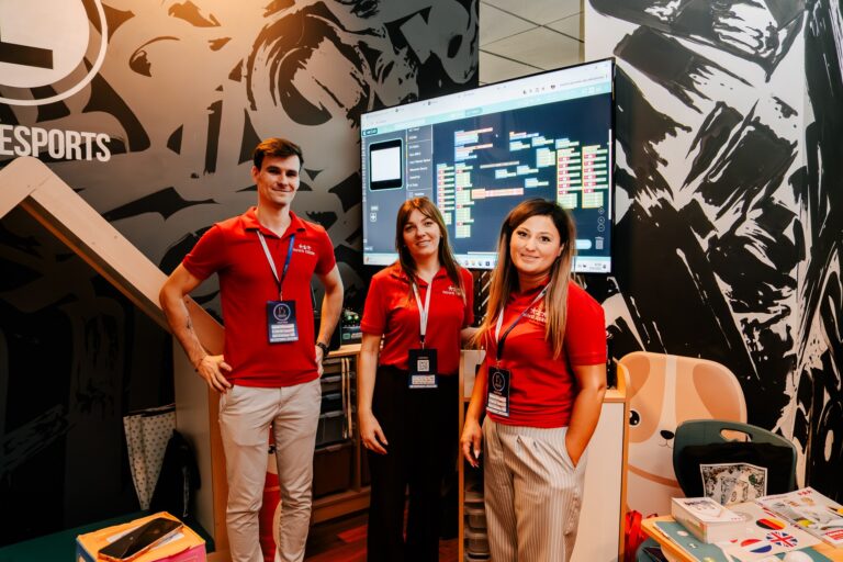 Zespół przedstawicieli firmy Nowa Szkoła podczas 15. Forum Rozwoju Mazowsza. Trzy osoby w czerwonych koszulkach stoją przed ekranem prezentującym interfejs do nauki programowania blokowego, promując edukacyjne rozwiązania z zakresu robotyki i nowych technologii dla szkół.