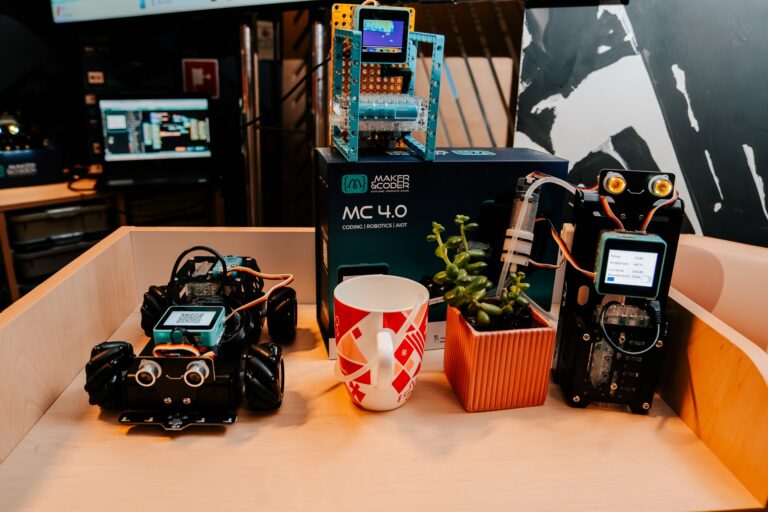 Prezentacja zestawu edukacyjnego Maker & Coder MC 4.0 podczas 15. Forum Rozwoju Mazowsza. Na stole znajdują się roboty edukacyjne, czujniki i układy elektroniczne wykorzystywane do nauki programowania, automatyki i Internetu Rzeczy (IoT). Obok robotów ustawiono kubek i doniczkę z rośliną, co nadaje aranżacji przyjazny, warsztatowy charakter