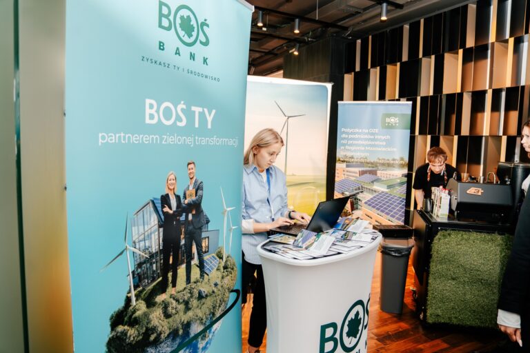 Stoisko BOŚ Banku podczas 15. Forum Rozwoju Mazowsza. Na banerze widnieje hasło „BOŚ TY – partnerem zielonej transformacji”. Przy stanowisku pracowniczka banku obsługuje laptop, a na ladzie ułożone są broszury i materiały informacyjne dotyczące finansowania inwestycji ekologicznych i odnawialnych źródeł energii.