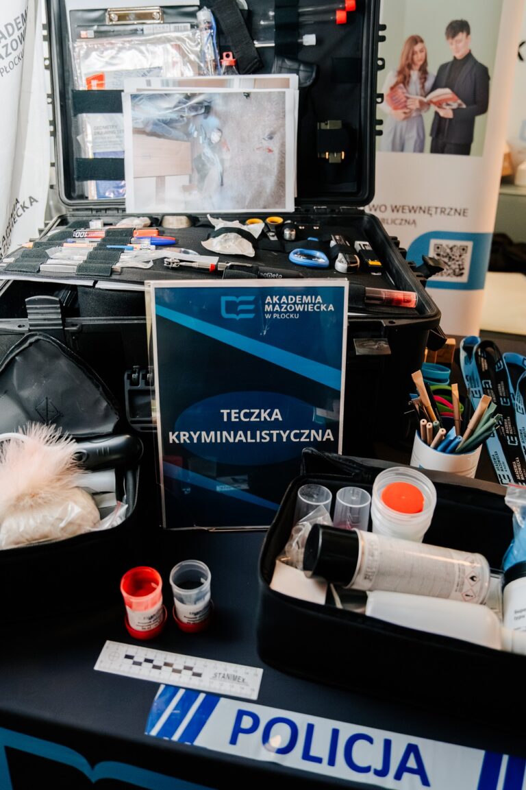 Stoisko Akademii Mazowieckiej w Płocku podczas 15. Forum Rozwoju Mazowsza. Na stole znajduje się zestaw kryminalistyczny z narzędziami i materiałami używanymi w pracy policyjnej, oznaczony tabliczką „Teczka kryminalistyczna”. W tle widoczny jest baner uczelni oraz materiały promocyjne kierunku bezpieczeństwa wewnętrznego.