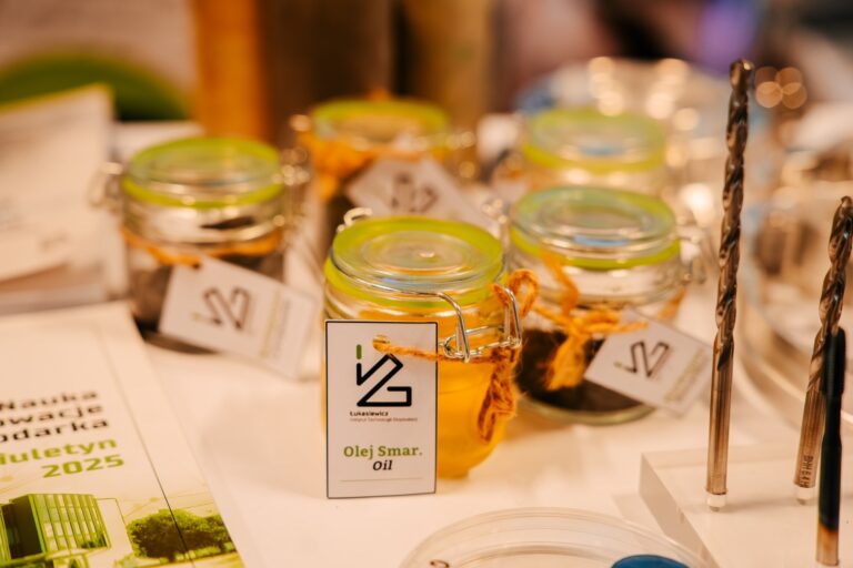 Stoisko Sieci Badawczej Łukasiewicz podczas 15. Forum Rozwoju Mazowsza. Na stole stoją szklane słoiczki z próbkami olejów i smarów oznaczone etykietą „Łukasiewicz – Instytut Technologii Eksploatacji”. Obok widoczne są metalowe wiertła i materiały promocyjne instytutu.