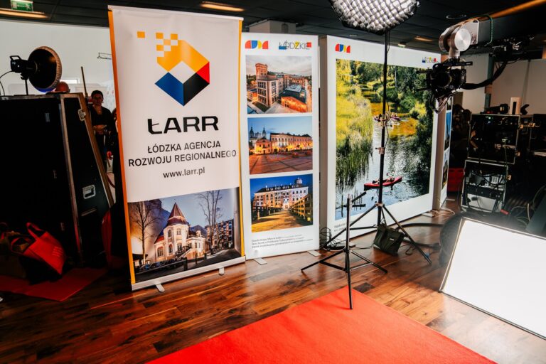 Stoisko Łódzkiej Agencji Rozwoju Regionalnego podczas 15. Forum Rozwoju Mazowsza. Na banerze widnieje logo LARR oraz zdjęcia przedstawiające architekturę i przyrodę regionu łódzkiego. Obok ustawione są lampy i sprzęt oświetleniowy do nagrań lub sesji zdjęciowej.