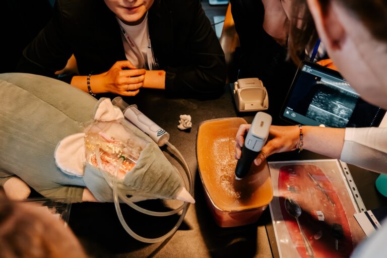 Uczestnicy 15. Forum Rozwoju Mazowsza obserwują demonstrację medyczną z użyciem głowicy USG i symulatora treningowego. Na stole widać sztuczny model organów oraz pluszowego szczura z elementami imitującymi układ nerwowy i naczyniowy.