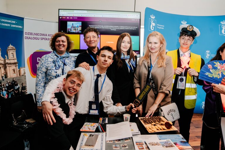 Grupa uczestników 15. Forum Rozwoju Mazowsza pozuje przy stoisku dzielnicy Targówek. Osoby uśmiechają się do zdjęcia, za nimi widać roll-upy informacyjne i ekran prezentacyjny.