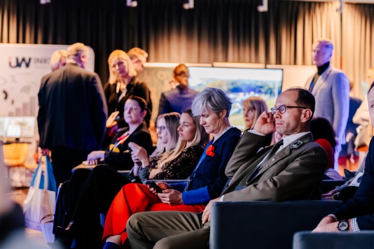 Uczestnicy 15. Forum Rozwoju Mazowsza siedzą na widowni podczas prezentacji. W pierwszym rzędzie widać osoby skupione na wystąpieniu, a w tle stoją inni uczestnicy wydarzenia.