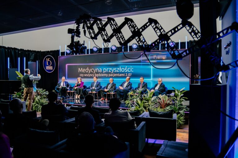 Uczestnicy debaty „Medycyna przyszłości: czy wszyscy będziemy pacjentami 2.0?” siedzą na scenie podczas 15. Forum Rozwoju Mazowsza. Przed nimi zgromadzona jest publiczność, a na scenie widoczny jest prowadzący stojący z mikrofonem. Tło stanowi duży ekran z tytułem dyskusji i logo wydarzenia, a scenę otaczają rośliny dekoracyjne.