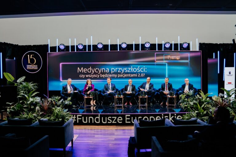 Siedmioro ekspertów bierze udział w debacie „Medycyna przyszłości: czy wszyscy będziemy pacjentami 2.0?” podczas 15. Forum Rozwoju Mazowsza. Uczestnicy siedzą na scenie przed dużym ekranem z tytułem dyskusji, a przed nimi ustawione są stoliki z wodą. Scenę otaczają rośliny dekoracyjne i podświetlony napis „#FunduszeEuropejskie”.