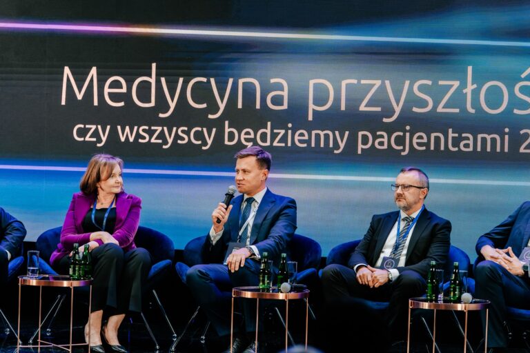 Uczestnicy debaty „Medycyna przyszłości: czy wszyscy będziemy pacjentami 2.0?” siedzą na scenie podczas 15. Forum Rozwoju Mazowsza. Mężczyzna w garniturze mówi do mikrofonu, a obok niego siedzą kobieta w fioletowej marynarce i mężczyzna w okularach. W tle widoczny jest ekran z tytułem dyskusji.