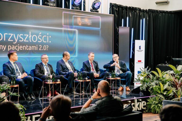 Paneliści biorą udział w debacie „Medycyna przyszłości: czy wszyscy będziemy pacjentami 2.0?” podczas 15. Forum Rozwoju Mazowsza. Siedzą na scenie przed dużym ekranem z tytułem dyskusji, a jeden z uczestników mówi do mikrofonu. Na pierwszym planie widownia, wokół sceny ustawione są rośliny dekoracyjne.