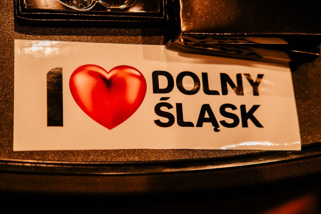Naklejka z napisem „I ❤️ Dolny Śląsk” leżąca na ciemnej powierzchni, sfotografowana podczas 15. Forum Rozwoju Mazowsza.